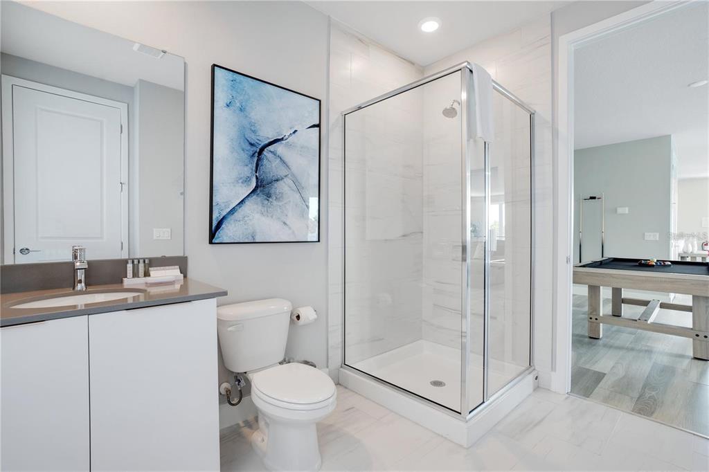 A bathroom features a glass-enclosed shower, a white toilet, and a vanity with a mirror — 7760 SANDY RIDGE DRIVE UNIT 200, REUNION, FL