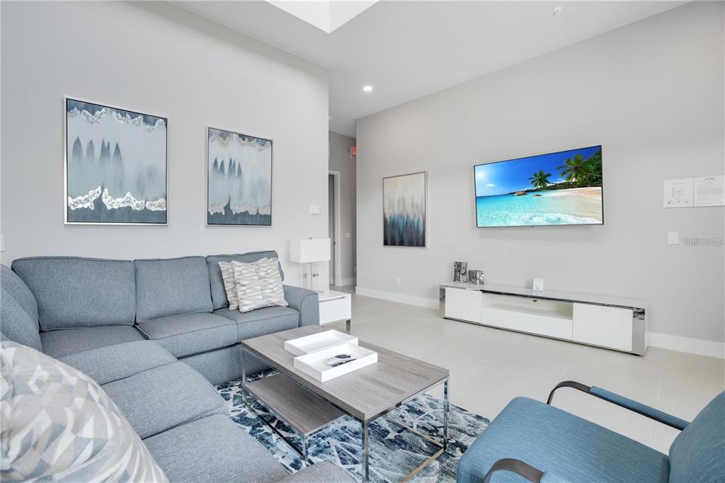 A modern living room features a grey sectional sofa, a coffee table, and a wall-mounted television — 7760 SANDY RIDGE DRIVE UNIT 200, REUNION, FL