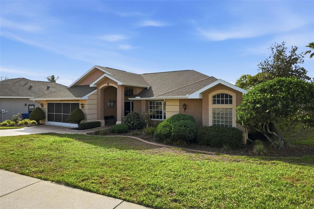 A single-story suburban house with a tan stucco exterior, a garage, and a landscaped yard — 13415 BOLTON COURT, SPRING HILL, FL