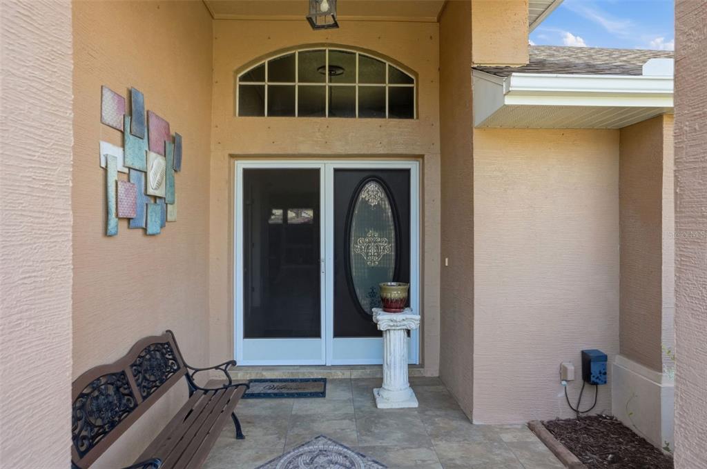 A covered entryway features a double door with a screen, a bench, and a pedestal planter — 13415 BOLTON COURT, SPRING HILL, FL