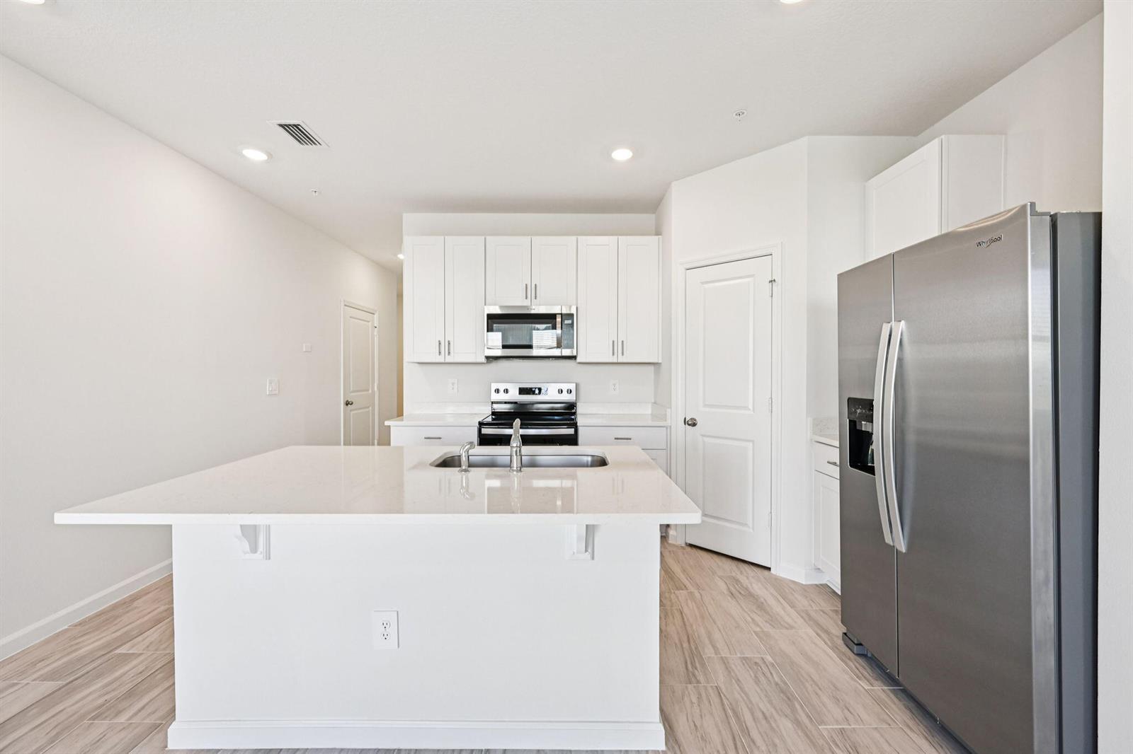 A modern kitchen features white cabinets, stainless steel appliances, a quartz island, and wood-look flooring — 632 Salisbury Circle, Fort Pierce FL 34982, FORT PIERCE, FL
