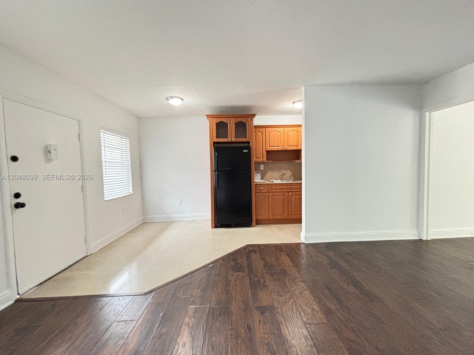 An interior view shows a kitchen with wood cabinets and a black refrigerator beside flooring — 1860 Venice Park Dr # 110, North Miami FL 33181, NORTH MIAMI, FL