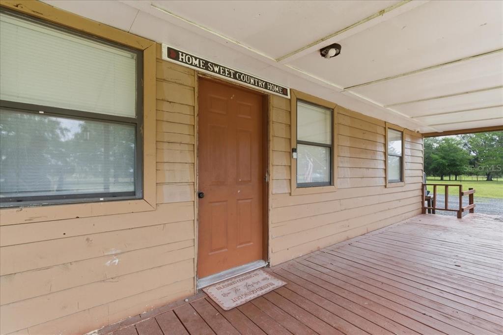 A covered wooden porch features a brown front door with a sign above it — 5040 RODEO DRIVE, KEYSTONE HEIGHTS, FL