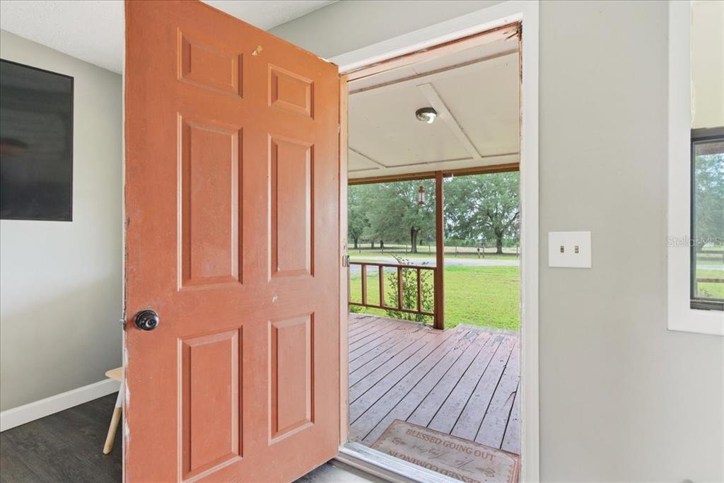 An open orange front door reveals a wooden porch overlooking a grassy yard with trees — 5040 RODEO DRIVE, KEYSTONE HEIGHTS, FL
