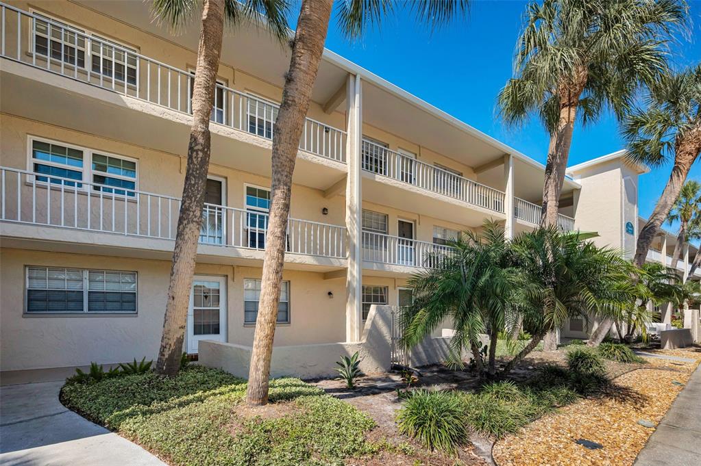 A three-story apartment building with balconies, palm trees, and a landscaped front yard — 936 VIRGINIA STREET UNIT 201, DUNEDIN, FL