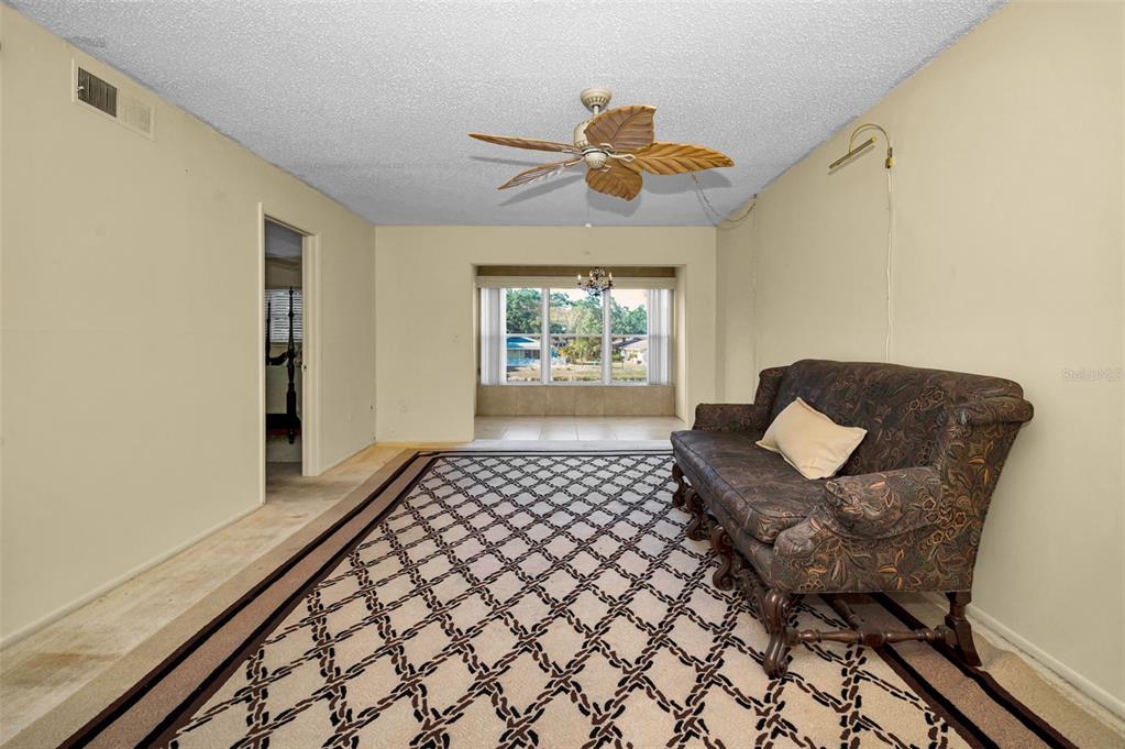 A living room features a patterned area rug, a dark patterned sofa, and a ceiling fan — 936 VIRGINIA STREET UNIT 201, DUNEDIN, FL