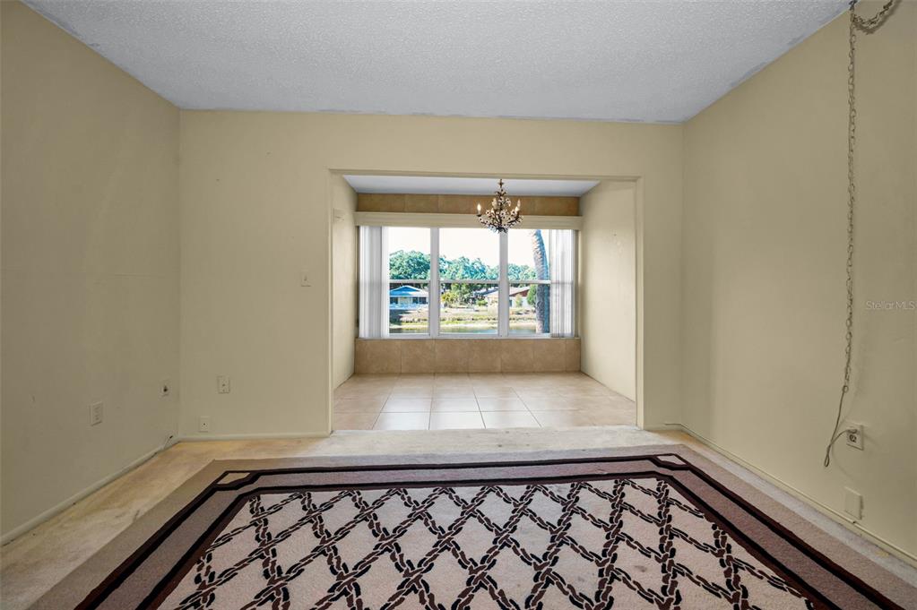 A carpeted living room opens into a tiled dining area with large windows overlooking water — 936 VIRGINIA STREET UNIT 201, DUNEDIN, FL