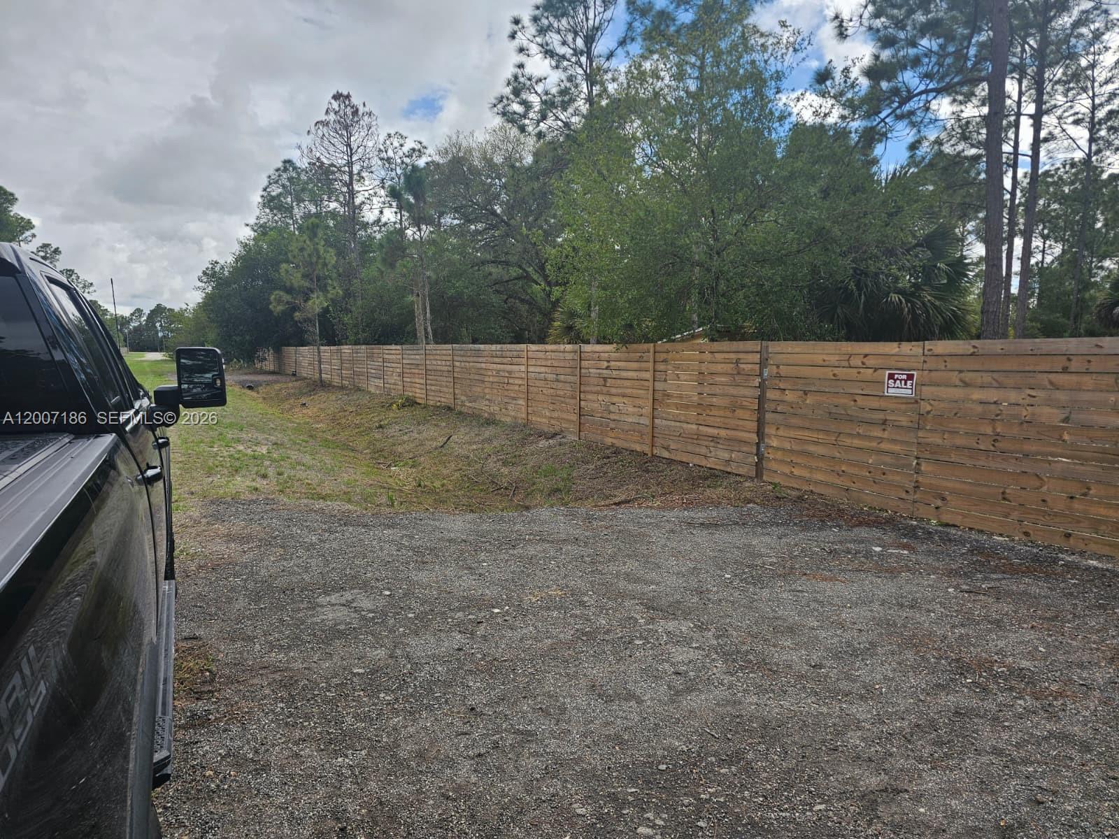 A gravel driveway runs alongside a long wooden fence bordering a wooded area — 820 & 830 S Jasmine Street, Clewiston FL 33440, CLEWISTON, FL