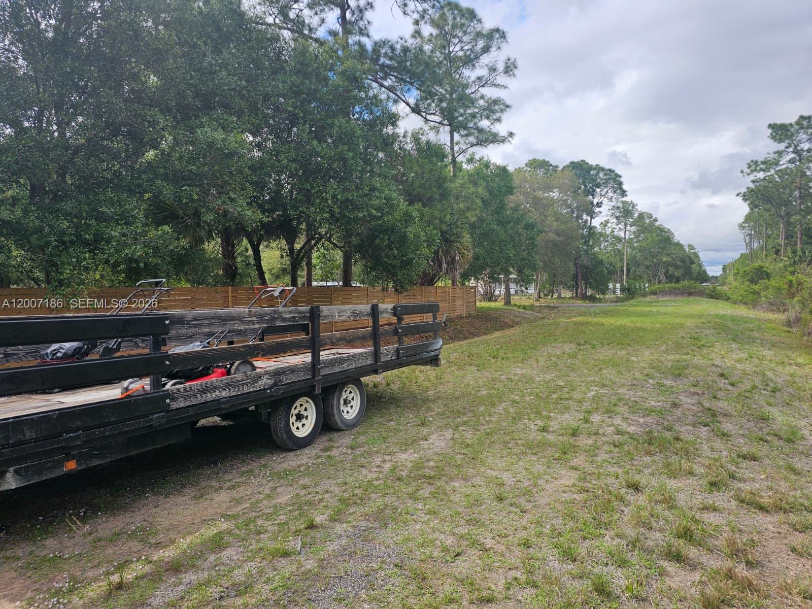A flat, grassy lot features a wooden fence and a utility trailer in the foreground — 820 & 830 S Jasmine Street, Clewiston FL 33440, CLEWISTON, FL