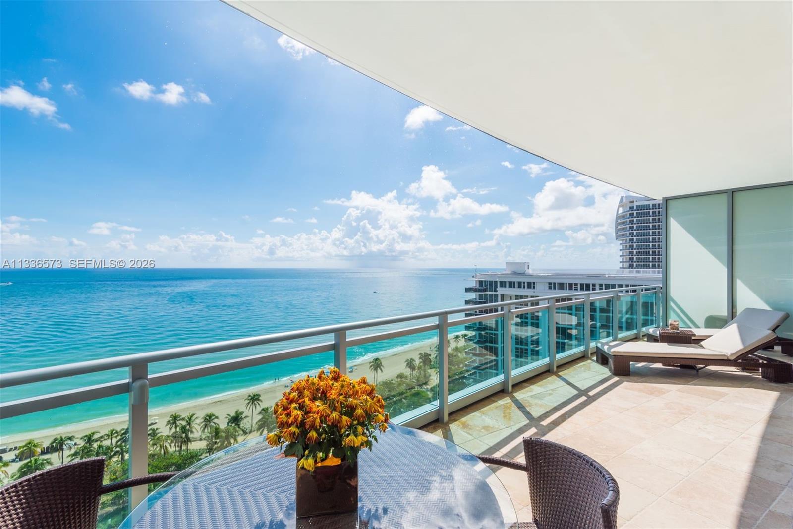 A balcony with a glass railing overlooks the ocean and a sandy beach — 10295 Collins Ave # 1202, Bal Harbour FL 33154, BAL HARBOUR, FL