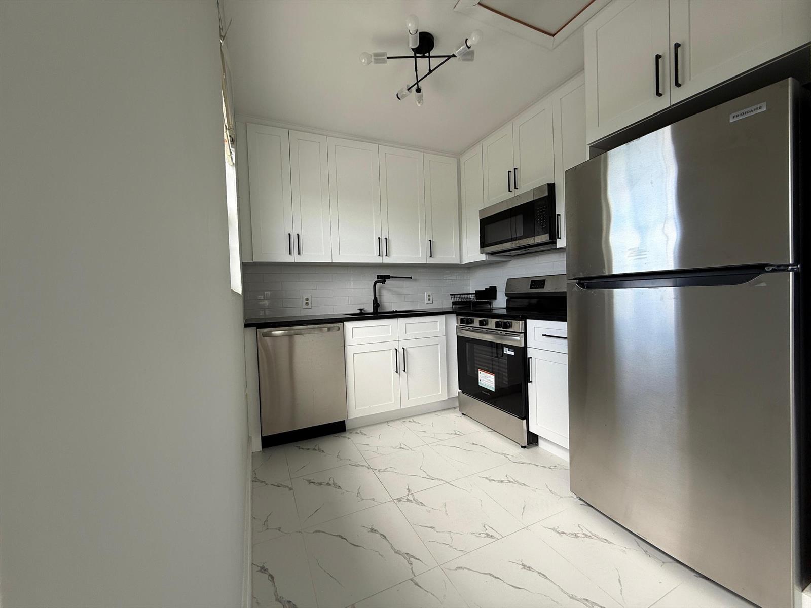 A kitchen features white cabinets, stainless steel appliances, black countertops, and white marble-patterned tile floors — 365 Brighton I # I, Boca Raton FL 33434, BOCA RATON, FL