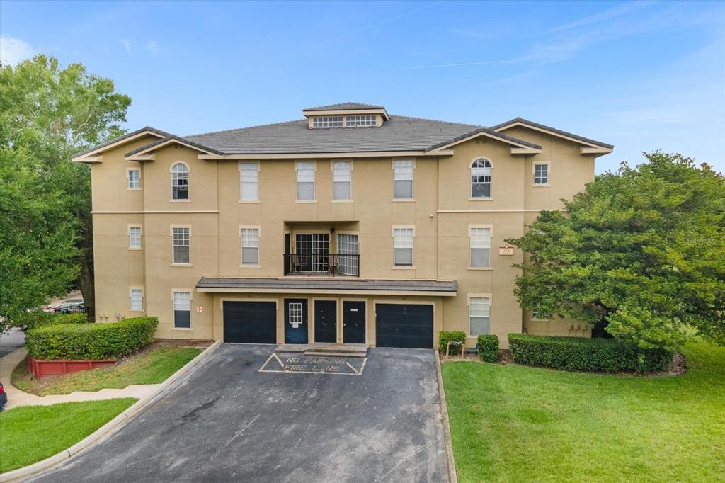 A three-story tan stucco apartment building with a black-roofed garage and a small balcony — 1341 ARBOR VISTA LOOP UNIT 317, LAKE MARY, FL