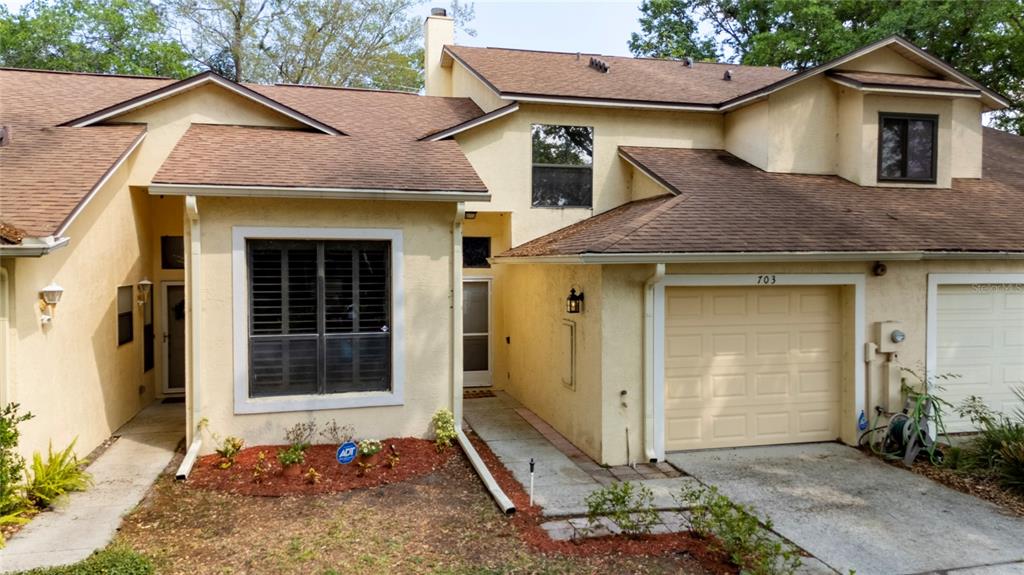 A two-story townhouse with a tan stucco exterior, brown shingled roof, and a single-car garage — 703 SWAN LANE, ALTAMONTE SPRINGS, FL