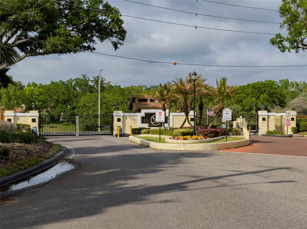 A gated entrance features a paved driveway, landscaping, and a security booth under a cloudy sky — 703 SWAN LANE, ALTAMONTE SPRINGS, FL
