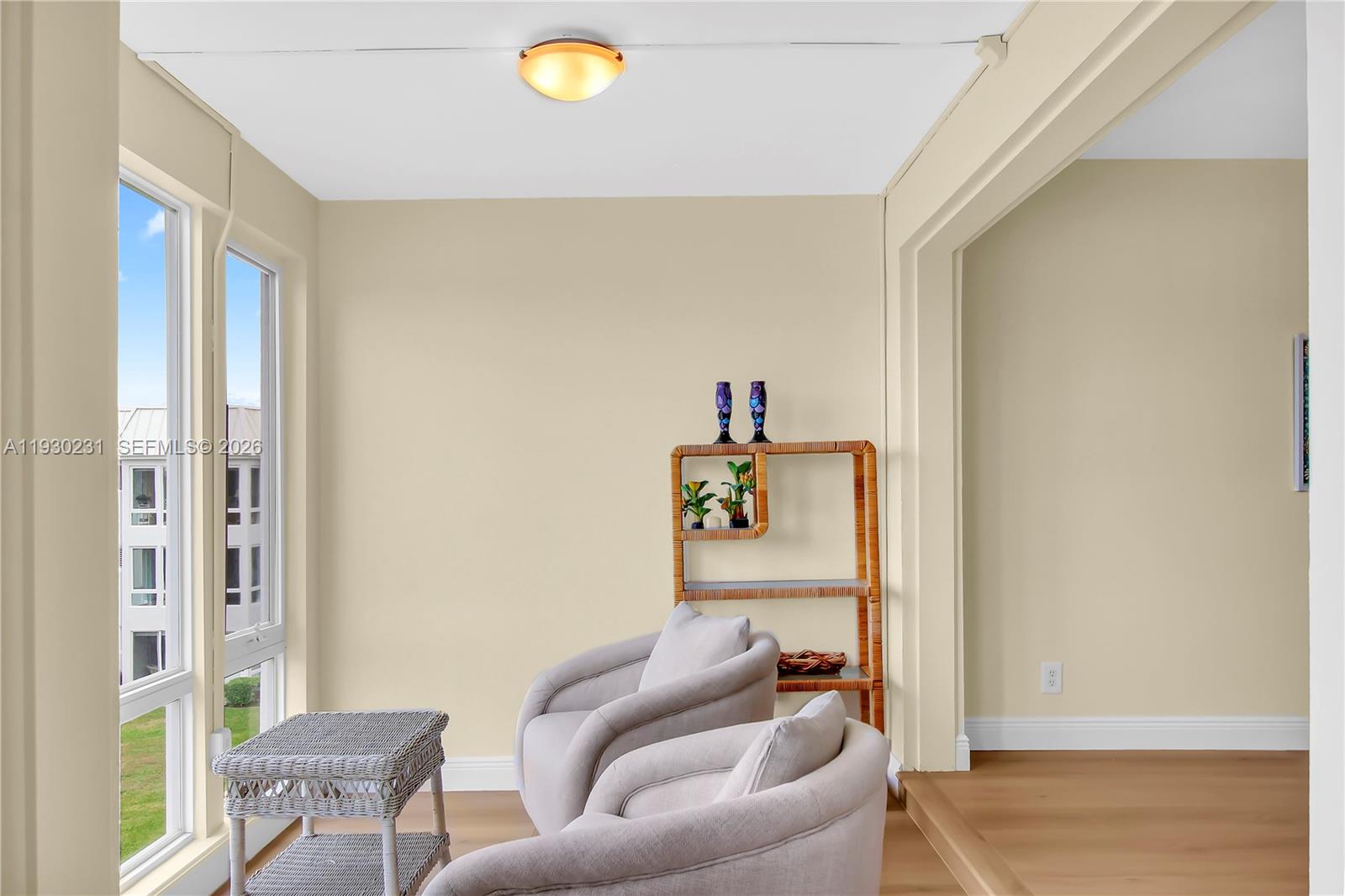 A sunroom features light-colored walls, wood flooring, two armchairs, a wicker table, and large windows — 7 Colonial Club Drive # 302, Boynton Beach FL 33435, BOYNTON BEACH, FL