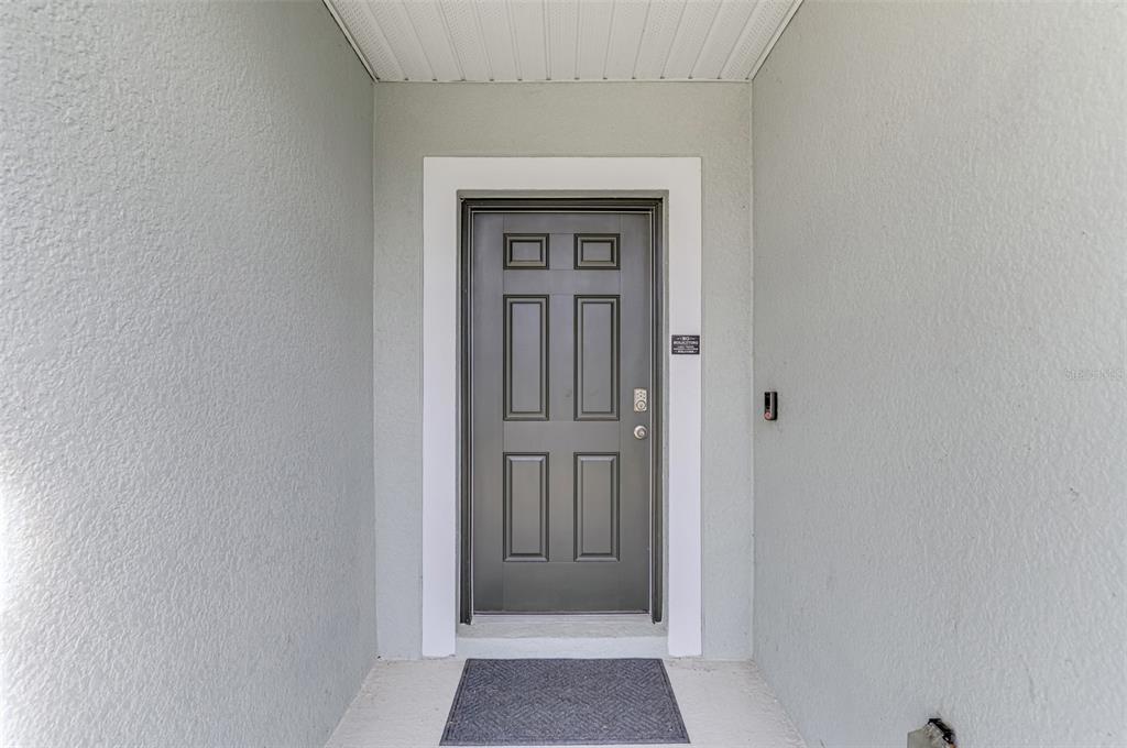 A gray front door with six panels is centered in a covered entryway — 25889 AYSEN DRIVE, PUNTA GORDA, FL