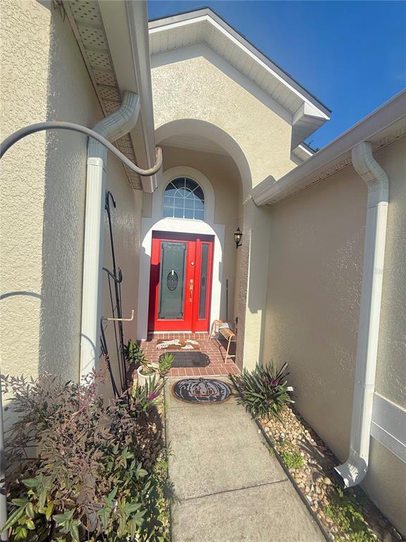 A red front door is recessed within an arched entryway featuring a concrete walkway — 733 SADDLE RIDGE DRIVE, DAVENPORT, FL