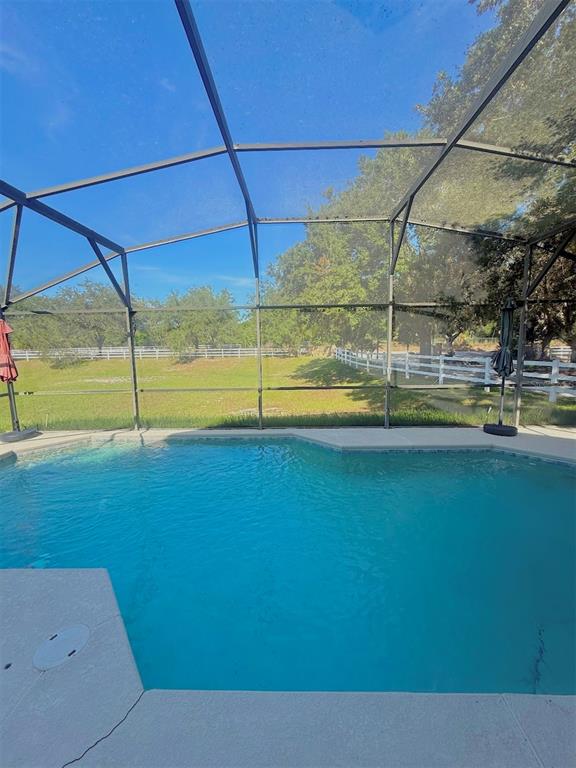 A swimming pool enclosed by a screen cage overlooks a grassy yard and white fence — 733 SADDLE RIDGE DRIVE, DAVENPORT, FL