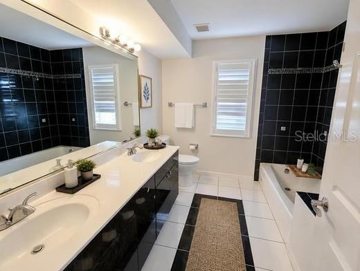 A bathroom features a double vanity, a soaking tub with black tile, and white floor tiles — 1343 UNDERHILL CIRCLE, PORT CHARLOTTE, FL
