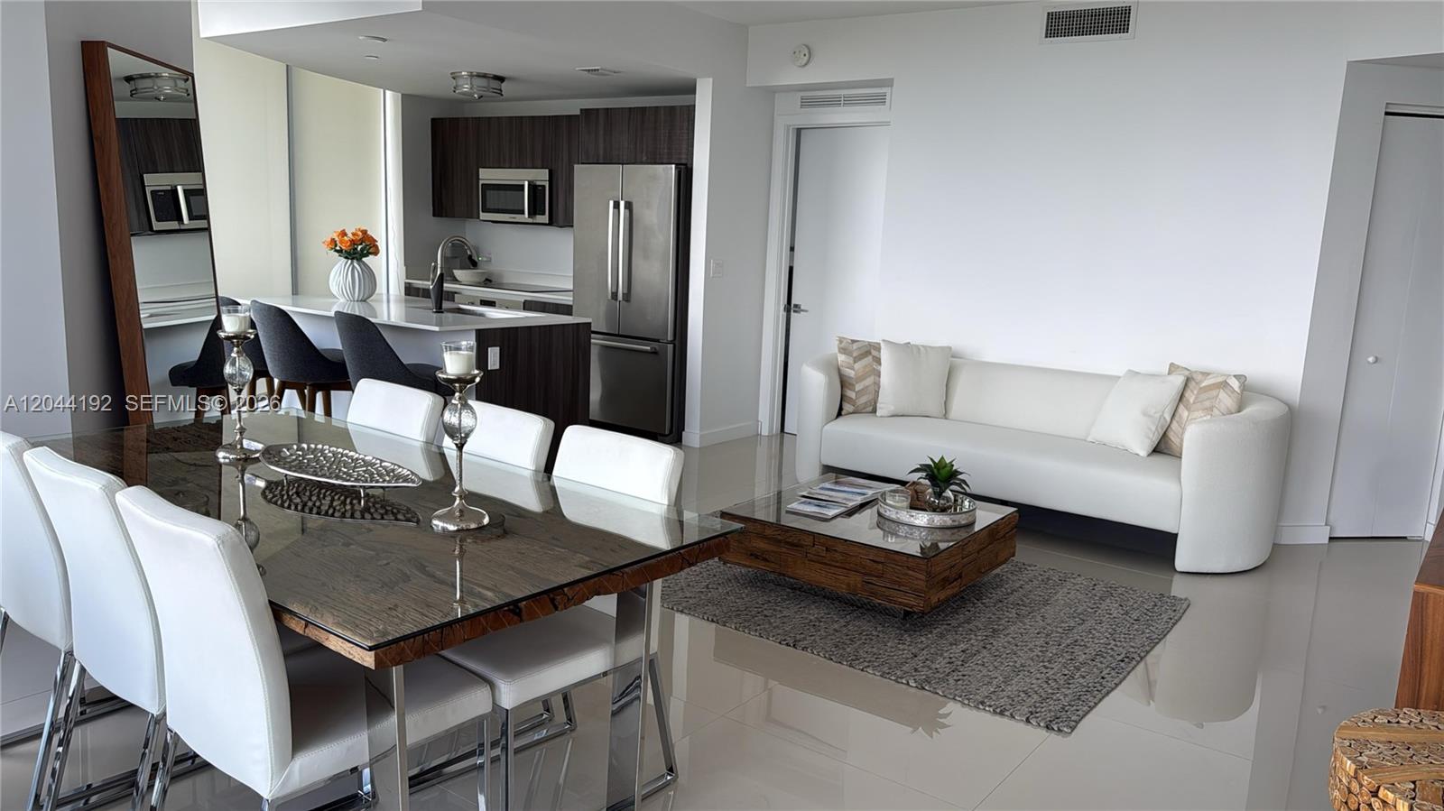 An open-concept living and dining area features a modern kitchen, white sofa, and glass-topped table — 488 NE 18th St # 2701, Miami FL 33132, MIAMI, FL
