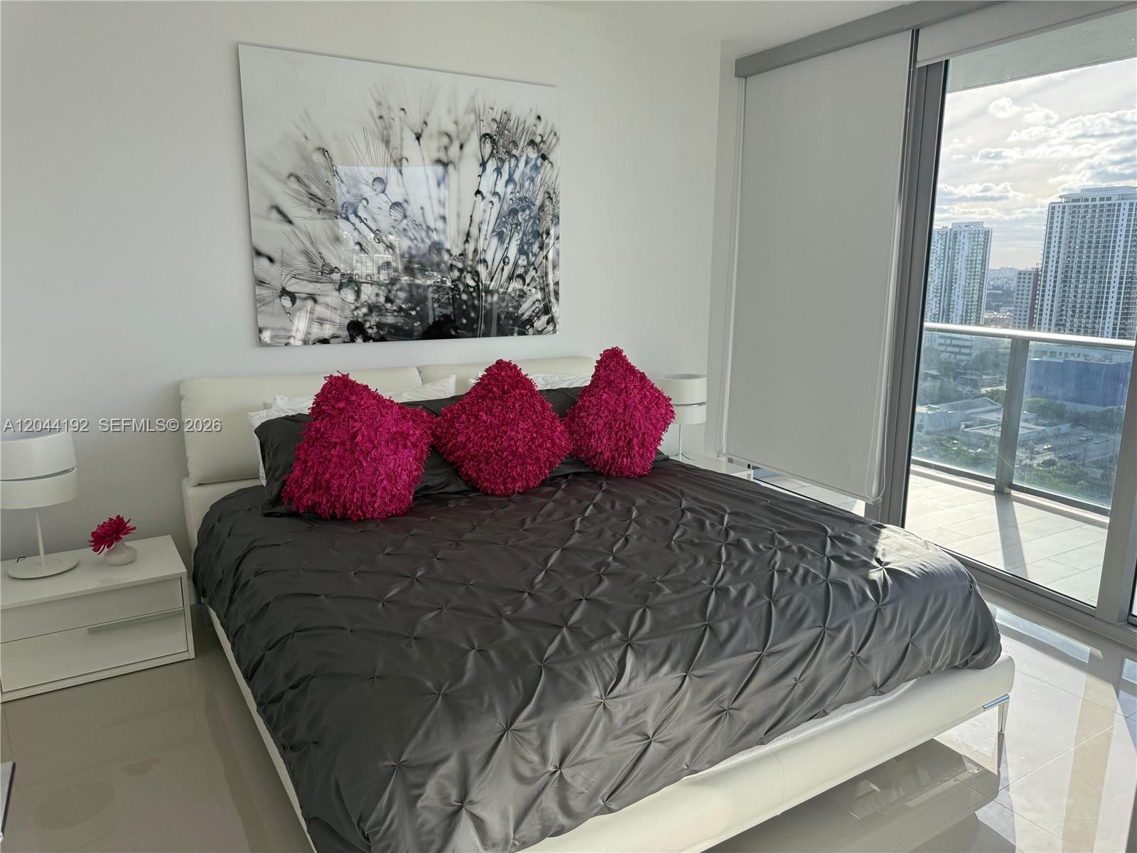 A modern bedroom features a tufted gray bed, bright pink pillows, and a city view — 488 NE 18th St # 2701, Miami FL 33132, MIAMI, FL