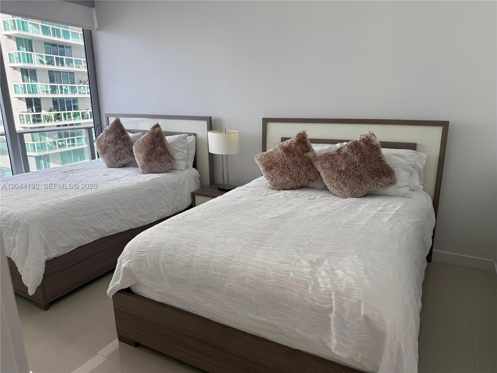 A bedroom features two beds with wood frames, textured pillows, and a city view outside — 488 NE 18th St # 2701, Miami FL 33132, MIAMI, FL