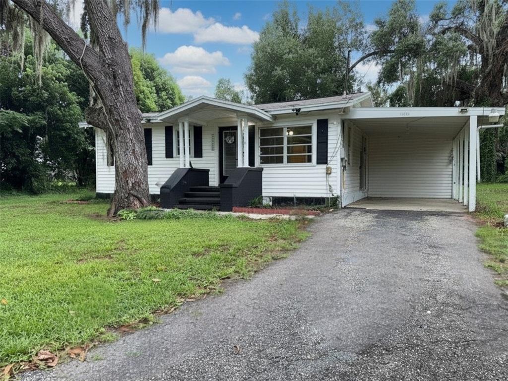 A white single-story house with a black front porch, a carport, and a large oak tree — 37318 CARTER AVENUE, DADE CITY, FL