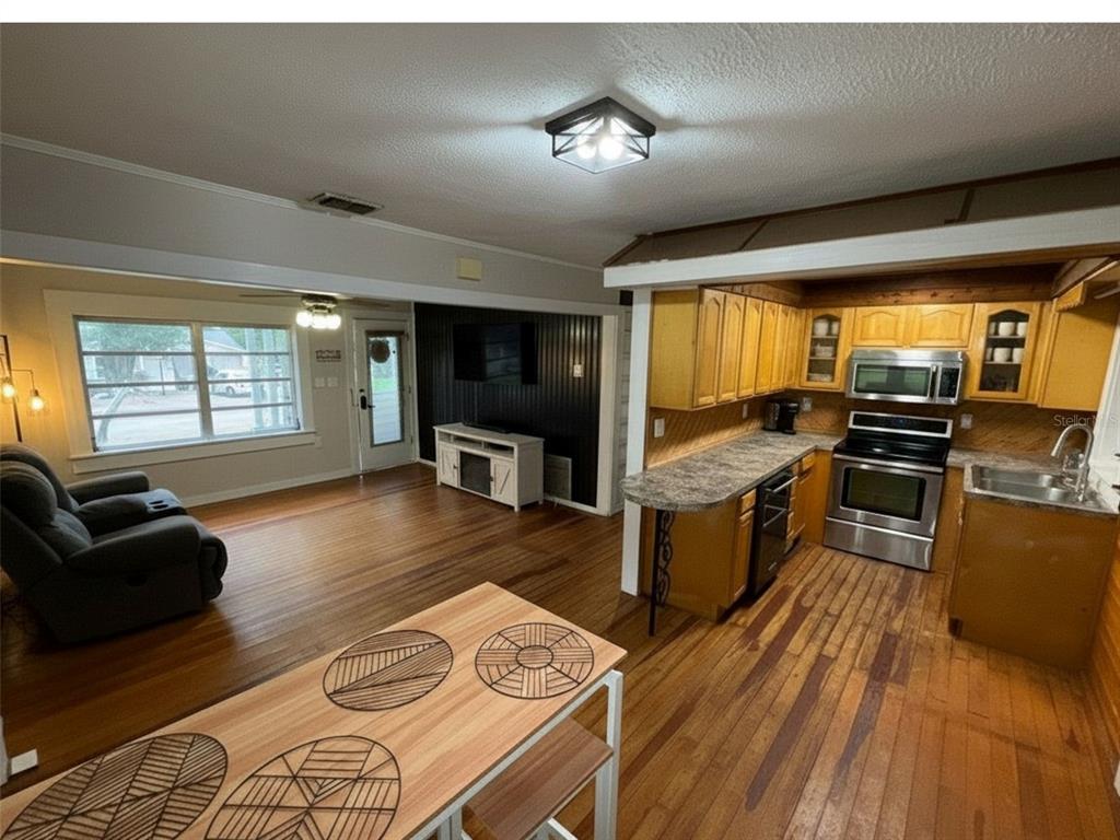 An open-concept kitchen and living area with wood flooring, wood cabinets, and stainless steel appliances — 37318 CARTER AVENUE, DADE CITY, FL