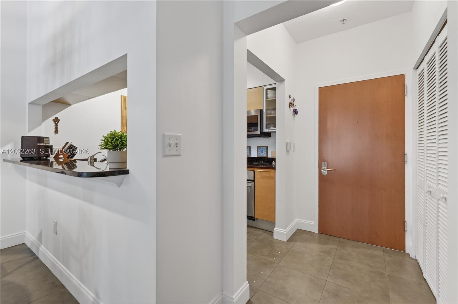A view of an entryway with a brown door, tiled floors, and a kitchen pass-through — 31 SE 5th St # 203, Miami FL 33131, MIAMI, FL