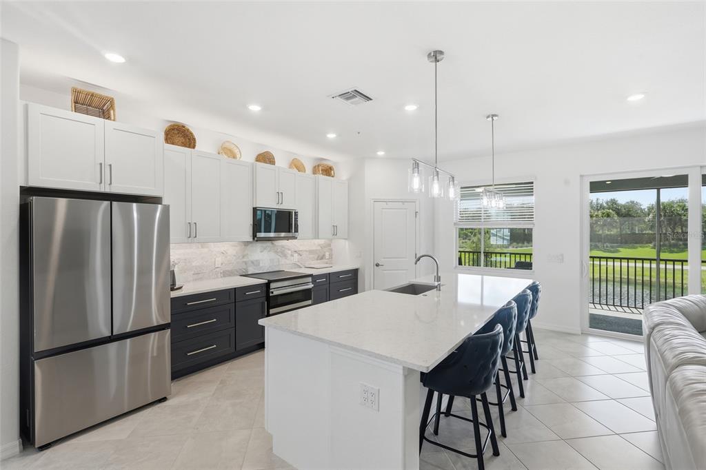 A modern kitchen features white upper cabinets, dark lower cabinets, a quartz island, and stainless appliances — 14842 BIRCHWOOD COURT UNIT 6521, PUNTA GORDA, FL