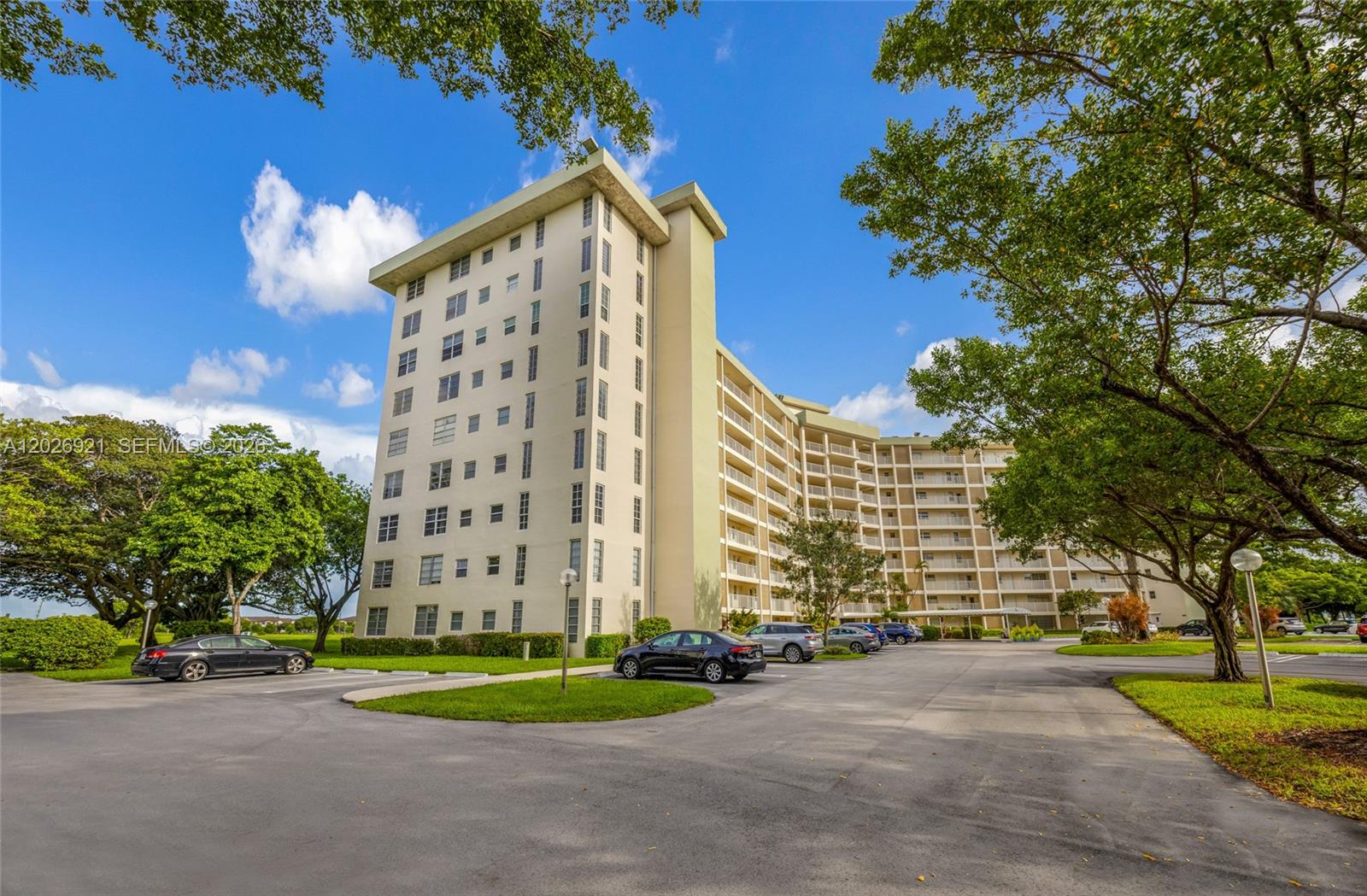 A multi-story apartment building stands next to a parking lot with several parked cars — POMPANO BEACH, FL