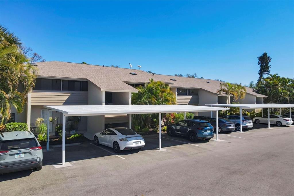 An exterior view of a multi-unit residential building with covered parking spaces and parked cars — 3363 CROSS CREEK DRIVE UNIT 3363, SARASOTA, FL