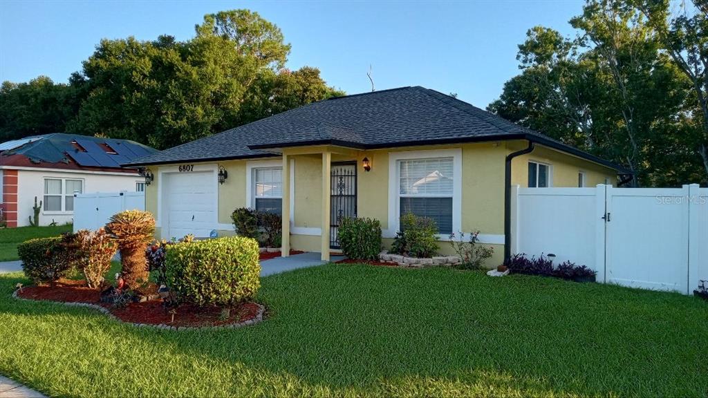 A yellow single-story house with a dark shingled roof and a white vinyl fence — 6807 KINGSTON DRIVE, TAMPA, FL
