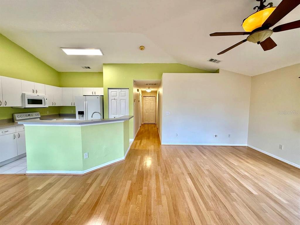 A kitchen with light green walls and wood flooring opens into a living area — 6807 KINGSTON DRIVE, TAMPA, FL