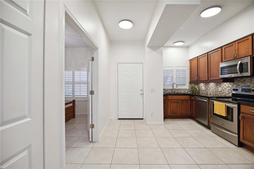 A kitchen with wood cabinets and stainless steel appliances opens into a tiled entryway — 4260 CENTRAL SARASOTA PARKWAY UNIT 213, SARASOTA, FL