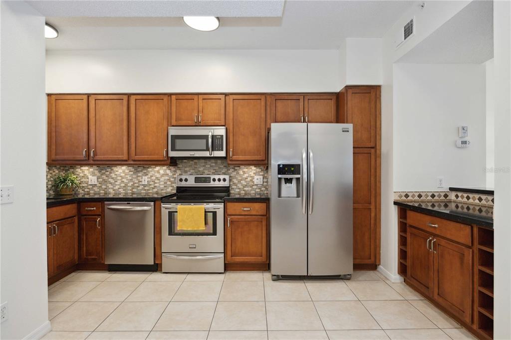 A kitchen features wood cabinets, stainless steel appliances, a tiled backsplash, and dark countertops — 4260 CENTRAL SARASOTA PARKWAY UNIT 213, SARASOTA, FL