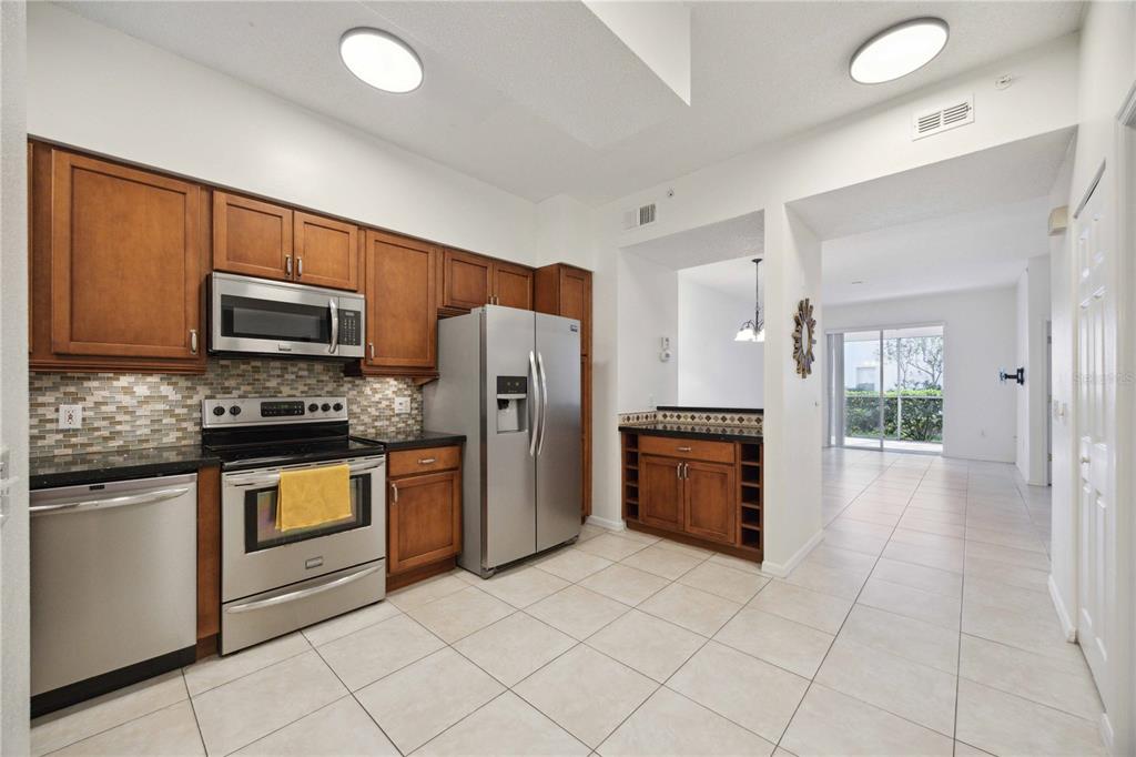 A kitchen features stainless steel appliances, wood cabinets, a tile backsplash, and light floor tiles — 4260 CENTRAL SARASOTA PARKWAY UNIT 213, SARASOTA, FL
