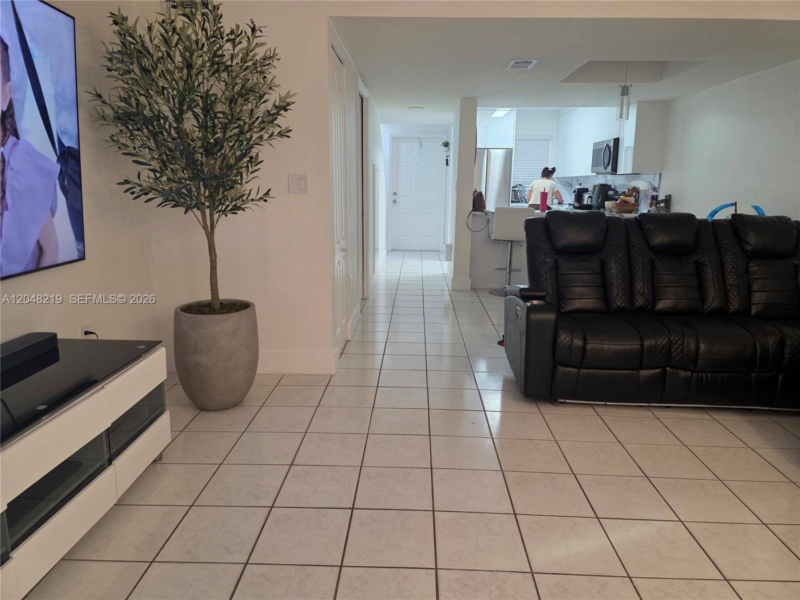 A living room with white tile floors, a black leather sofa, and an artificial tree — 523 W 68th St # 5, Hialeah FL 33014, HIALEAH, FL