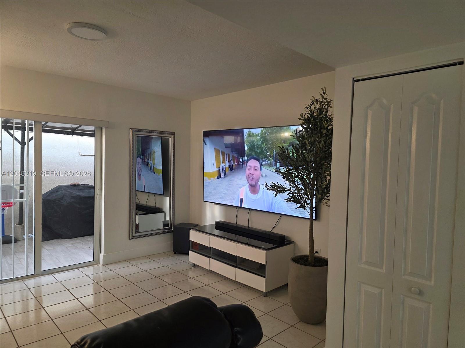 A living room features a wall-mounted television, a media console, a potted tree, and tile flooring — 523 W 68th St # 5, Hialeah FL 33014, HIALEAH, FL