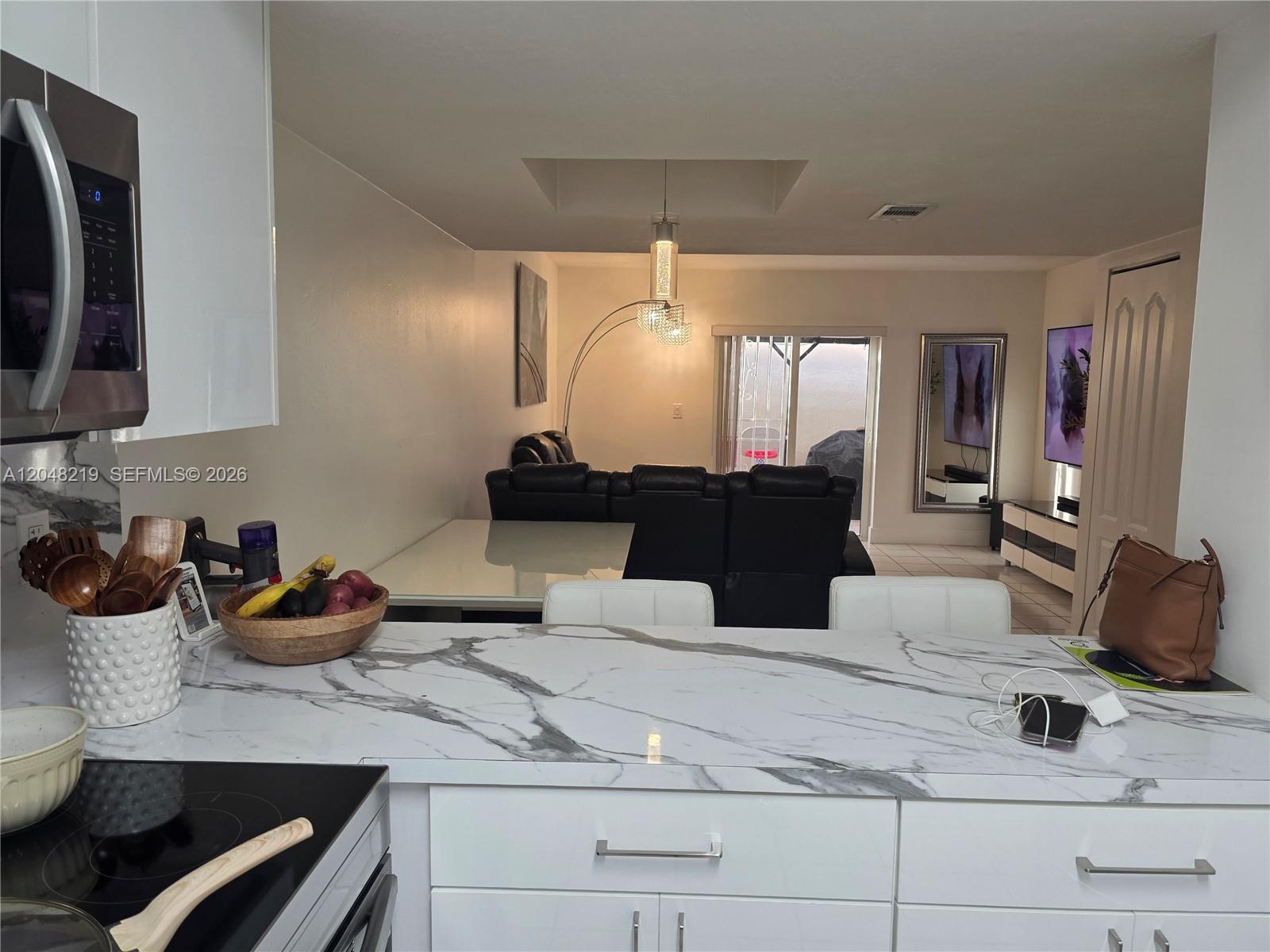A kitchen with a marble-patterned island overlooks a living room with black leather furniture — 523 W 68th St # 5, Hialeah FL 33014, HIALEAH, FL