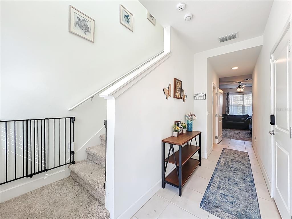 A carpeted staircase with a safety gate sits beside a tiled hallway with a console table — 1371 CAPTIVA COVE, SANFORD, FL