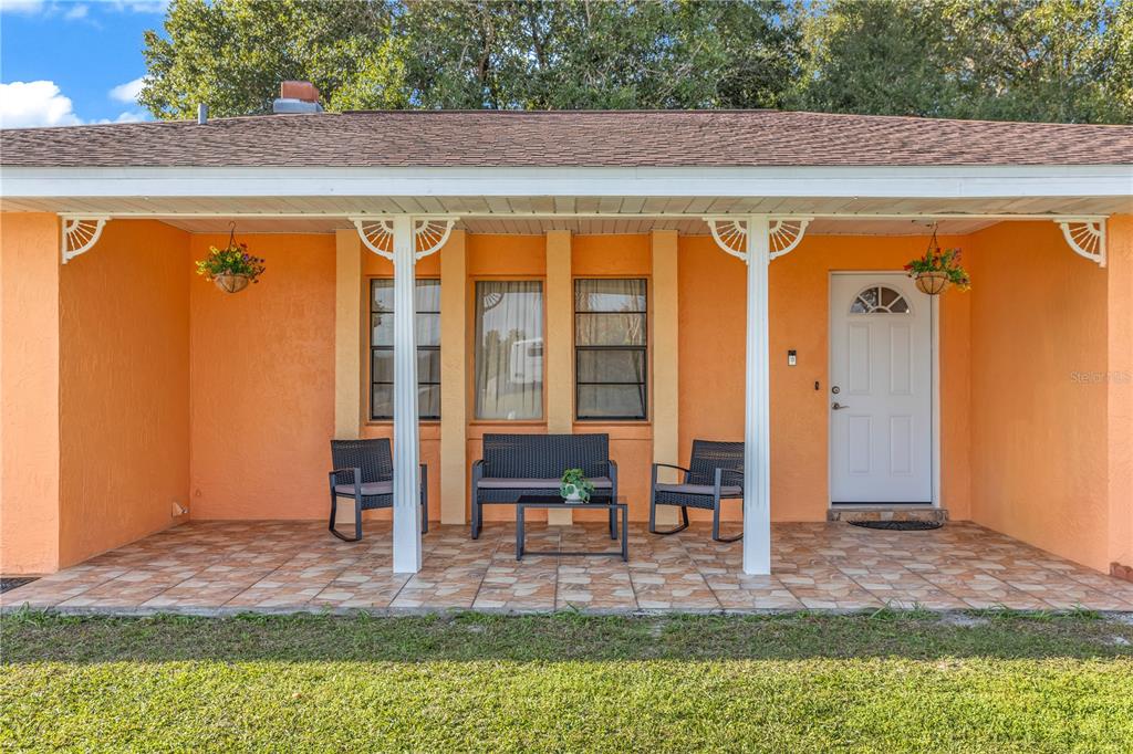 A covered front porch with tiled flooring features a bench, two chairs, and orange walls — 1642 HORSESHOE TERRACE, DELTONA, FL