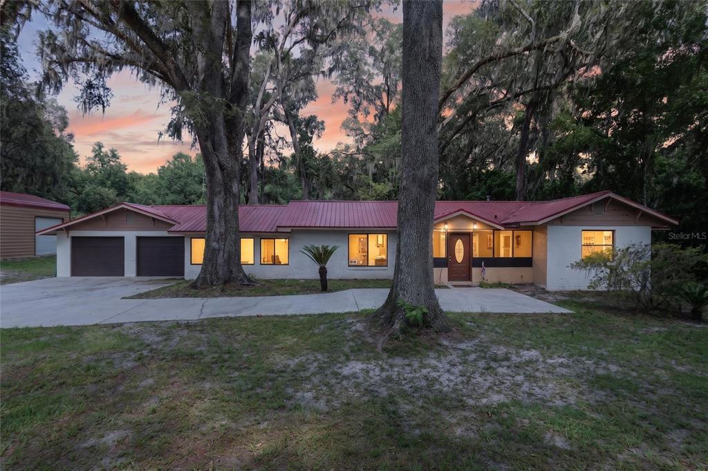 A single-story house with a red metal roof and a two-car garage sits among trees — 18741 N US HIGHWAY 301, CITRA, FL