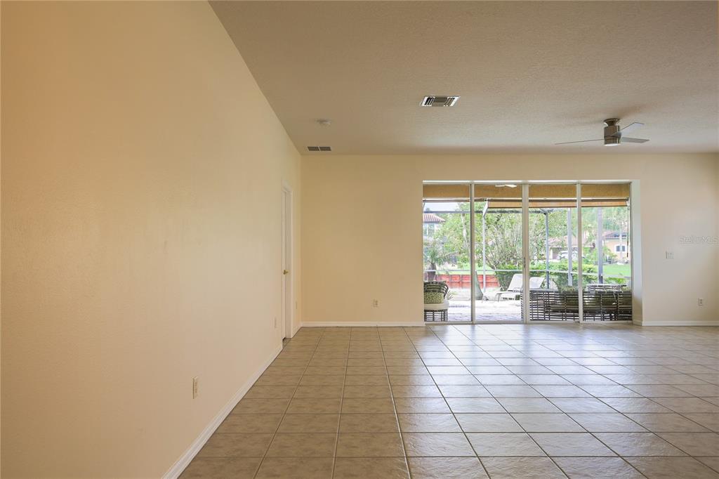An empty room features light-colored tile flooring, beige walls, and a large sliding glass door — 18014 JAVA ISLE DRIVE, TAMPA, FL