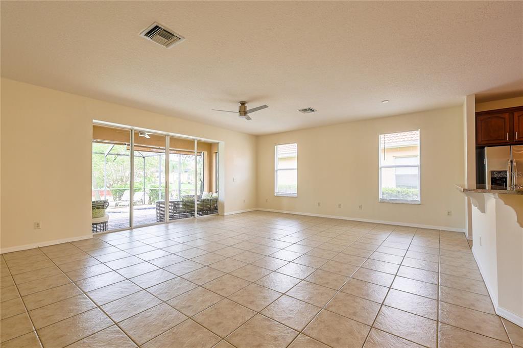 An empty living room features beige tile flooring, light-colored walls, and a sliding glass door — 18014 JAVA ISLE DRIVE, TAMPA, FL