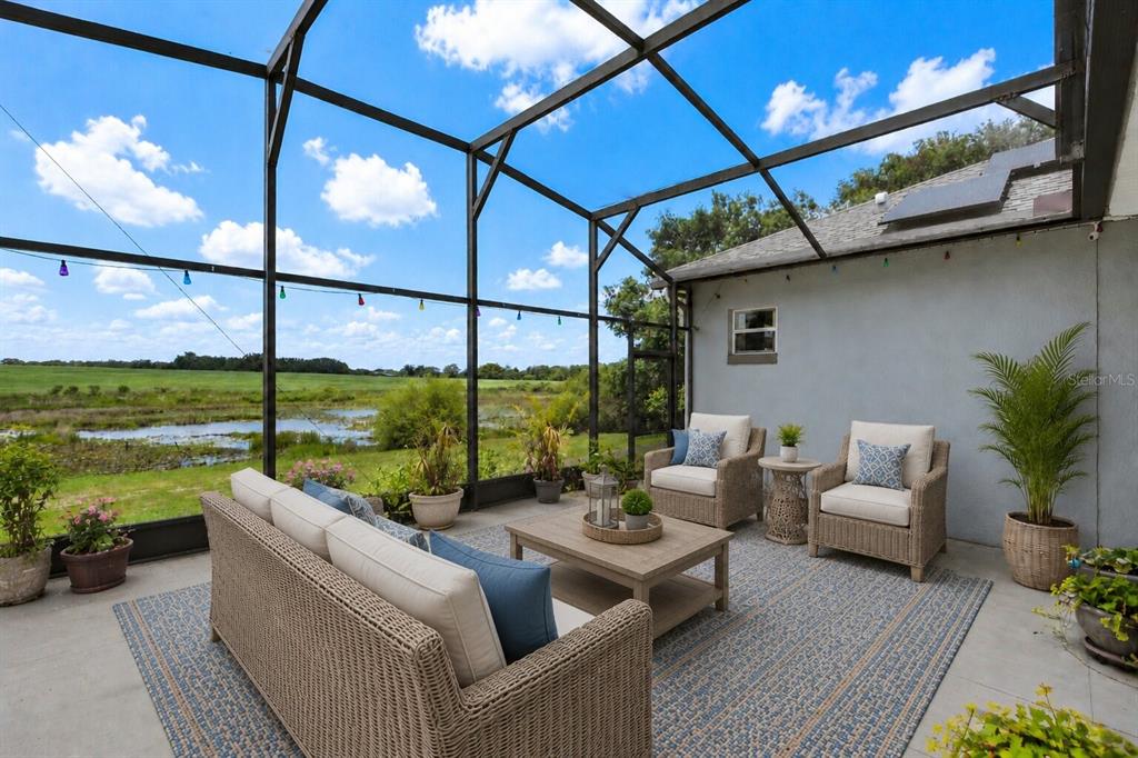 A screened-in patio features wicker furniture, a coffee table, and a view of a pond — 25501 MAUREPAS LANE, LEESBURG, FL