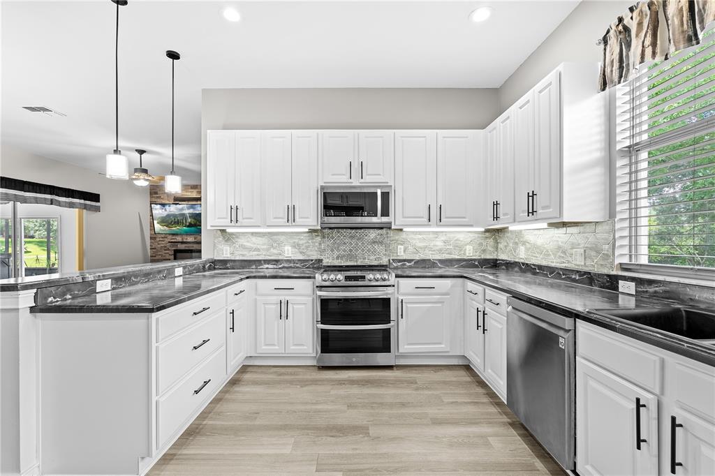 A kitchen features white cabinets, dark marble countertops, stainless steel appliances, and light wood flooring — 25501 MAUREPAS LANE, LEESBURG, FL