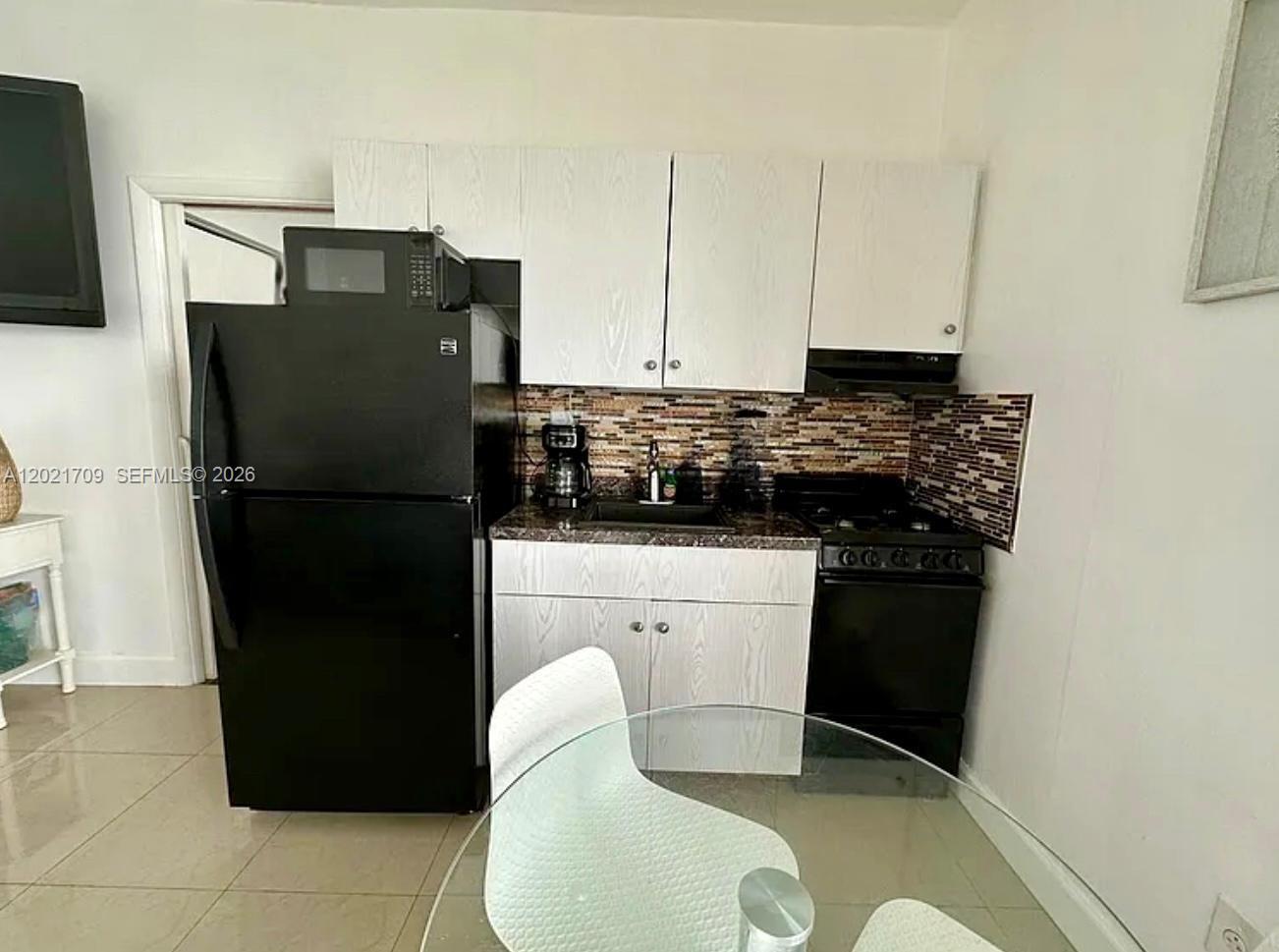 A small kitchen features white cabinets, black appliances, and a mosaic tile backsplash — 3700 Collins Ave # 306, Miami Beach FL 33140, MIAMI BEACH, FL