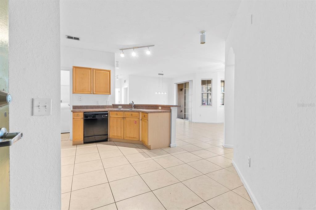 A kitchen with light wood cabinets and black appliances opens into a tiled living area — 707 TERRACE RIDGE CIRCLE UNIT 707, DAVENPORT, FL