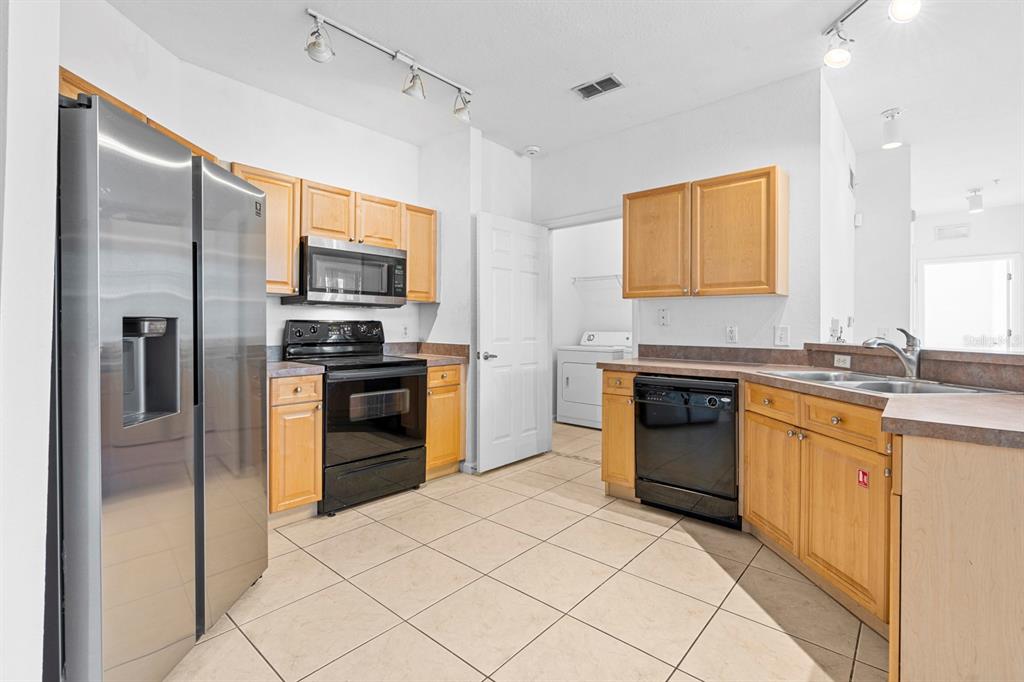 A kitchen features light wood cabinets, stainless steel appliances, and beige tile flooring — 707 TERRACE RIDGE CIRCLE UNIT 707, DAVENPORT, FL